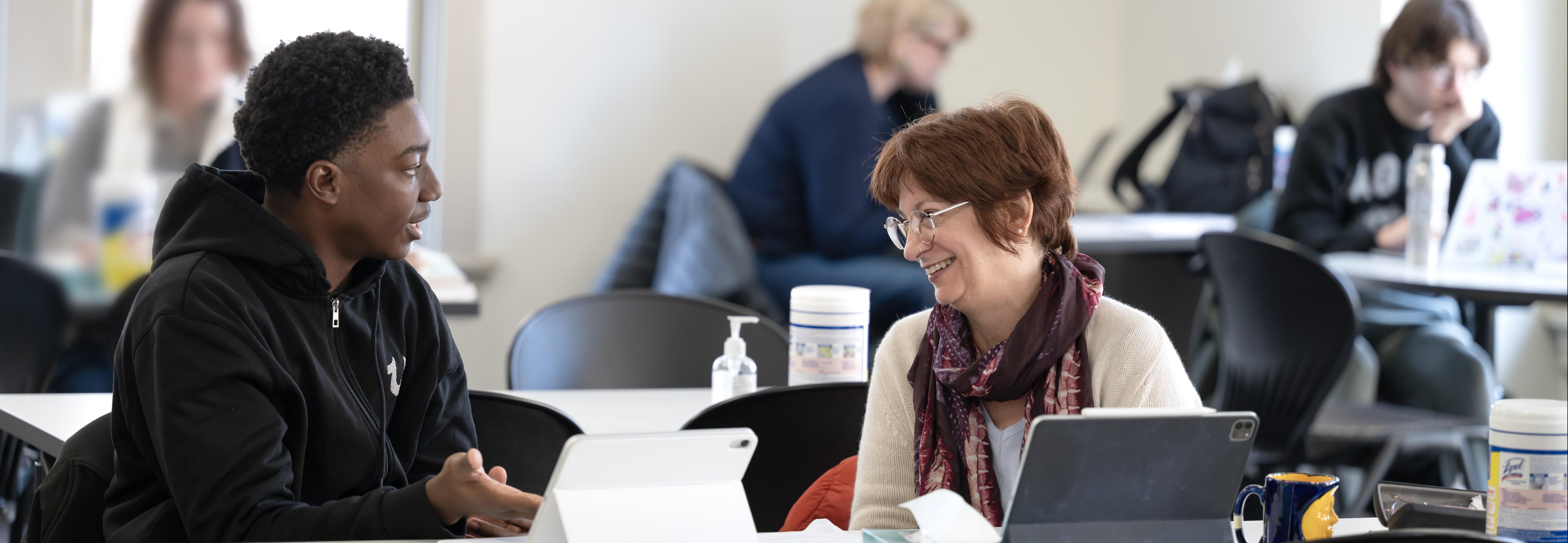 A writing consultant works with a student writer at the Writing Center. They are seated at a table.