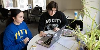 Two students work together on a laptop sitting on a table