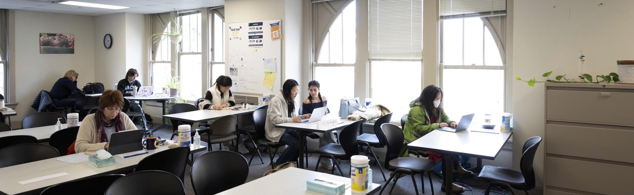 Faculty consultants and student writers work in the Writing Center, which is an open floor concept with tables and chairs where people are seated.